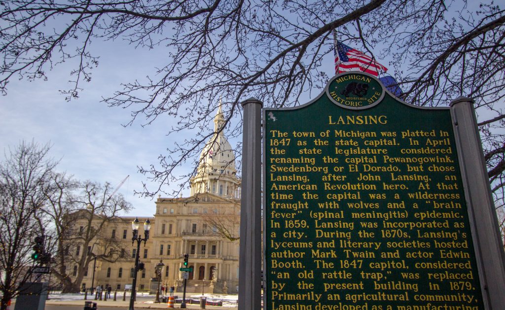 Lansing, Michigan, USA - January 20, 2018: Historical marker regarding the founding of Lansing and the Michigan state capitol building in the background.
